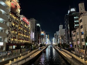 Une vue nocturne d’une rivière bordée de bâtiments des deux côtés, dont un hôtel appelé « HOTEL BAIL » et un restaurant à la façade colorée.