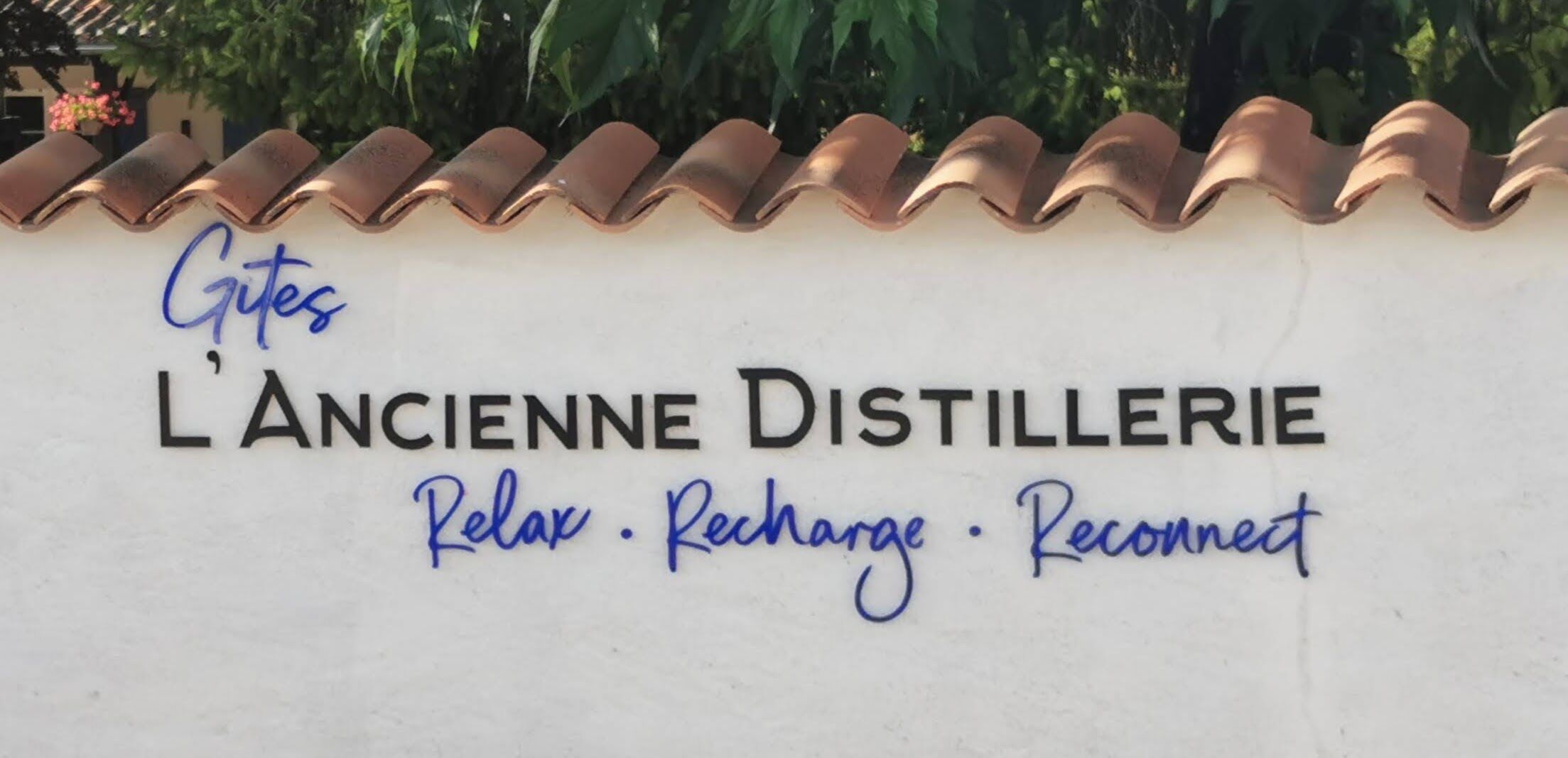 Een bord voor L'Ancienne Distillerie, met de tekst 'Relax · Opladen · Verbinden' onder de naam.
