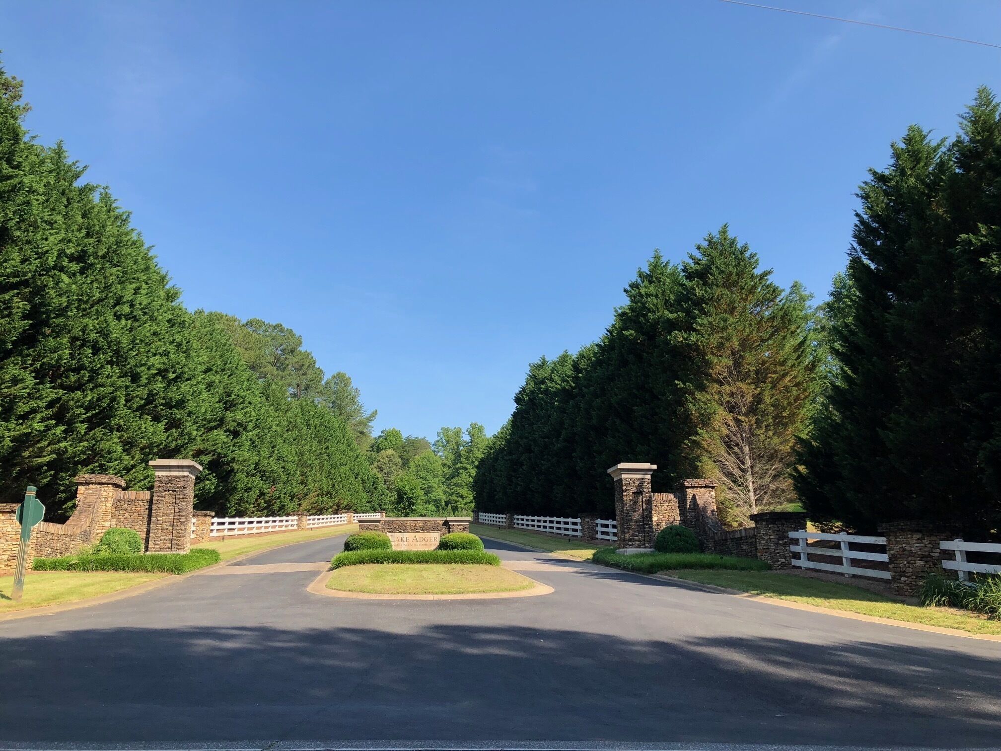 A driveway leading to a gated entrance with stone pillars and a white fence.