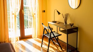 A room with a bed, a desk with a chair, a hanging light fixture, and a wall-mounted mirror.