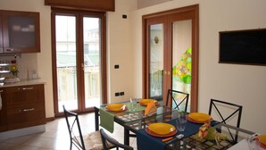 A dining area with a glass table, chairs, and yellow plates. There is a kitchen area with cabinets and a sink.