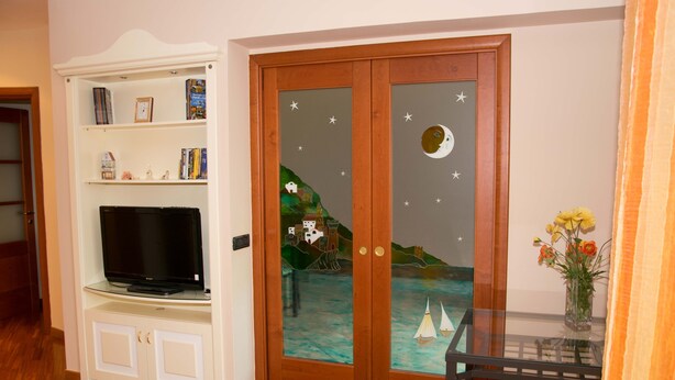 A room with a wooden cabinet containing a television, a glass door with a nautical scene, and a small table with a vase of flowers.