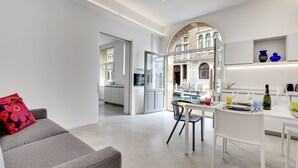A modern kitchen with white cabinetry, a dining area with a white table and chairs, and a red floral pillow on a grey sofa. - LADY T Luxury Loft, up to 14 people (Venezia)