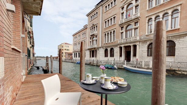 A table with a view of a canal, a wooden deck, and a building with arched windows and balconies. - LADY T Luxury Loft, up to 14 people (Venezia)