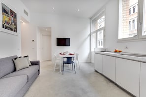 A modern apartment with a grey sofa, a dining table with chairs, a kitchen area, and a TV mounted on the wall. - LADY T Luxury Loft, up to 14 people (Venezia)