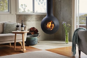 A cozy living room with a modern fireplace, a sofa, a small table with a wine bottle and glass, and a vase with flowers.