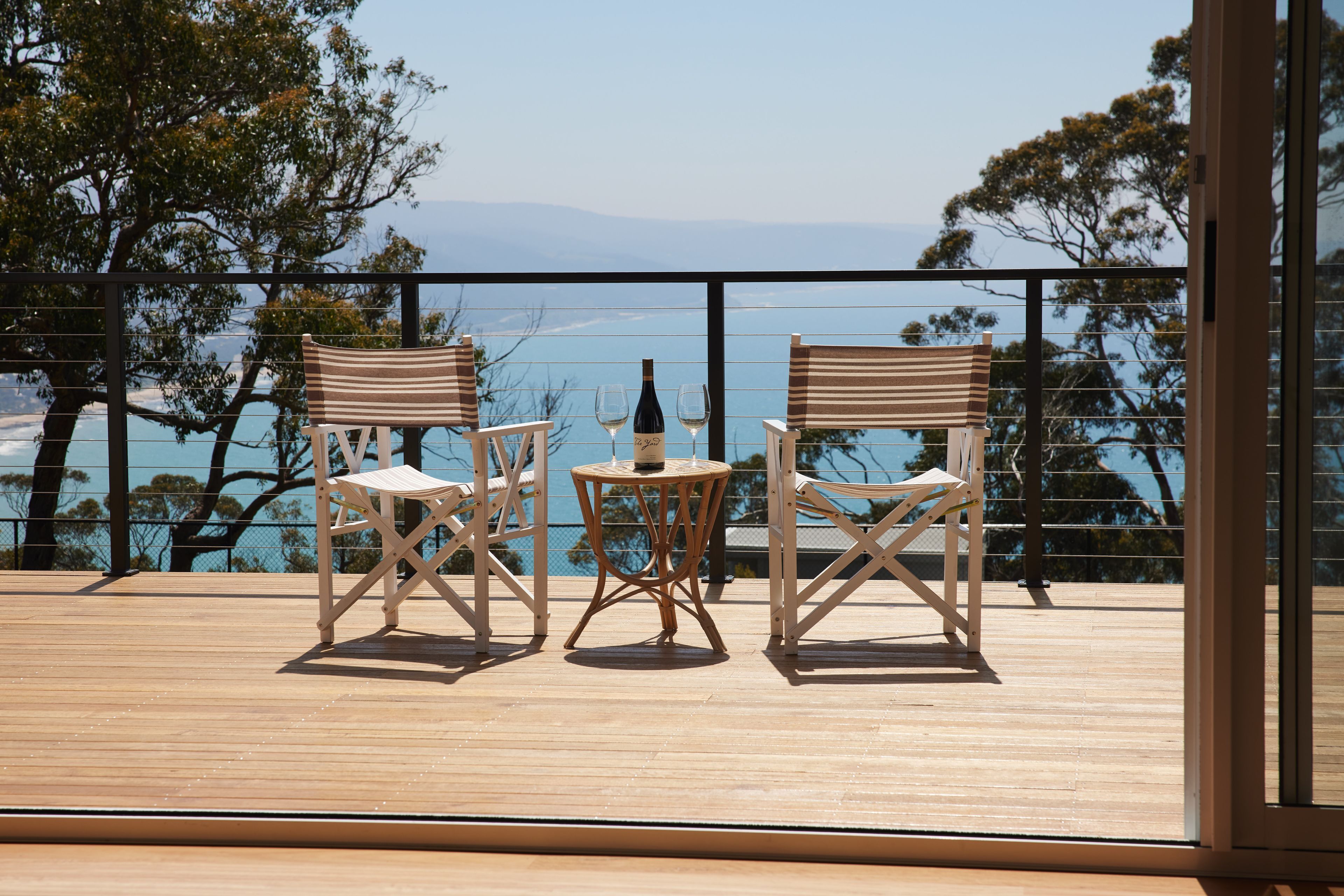 Terraza con dos sillas y una mesa, con vistas a un cuerpo de agua y árboles.
