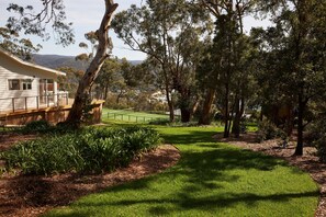 Una proprietà residenziale con un prato curato, un campo da tennis e un grande albero sullo sfondo.