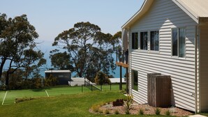 A house with a tennis court, a wooden fence, and a view of the sea.