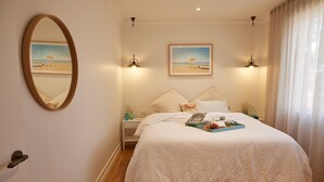A bedroom with a large bed, a nightstand, a mirror, two wall-mounted lights, and two framed pictures.