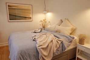 A neatly made bed with a blanket, pillows, and a bedside table with a book and a vase of dried flowers. - The White House Ocean Views Tennis Court in Lorne (Lorne)
