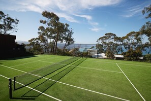 Campionat de tennis amb xarxa, envoltat d'arbres i vista al mar.
