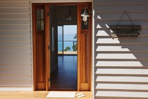 A wooden door leading to a balcony with a view of the sea, a hanging light fixture, and a sign indicating the property name and address.