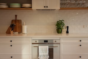 A kitchen with white cabinets, a wooden cutting board, a roll of paper towels, a green plant, and a digital oven control panel.