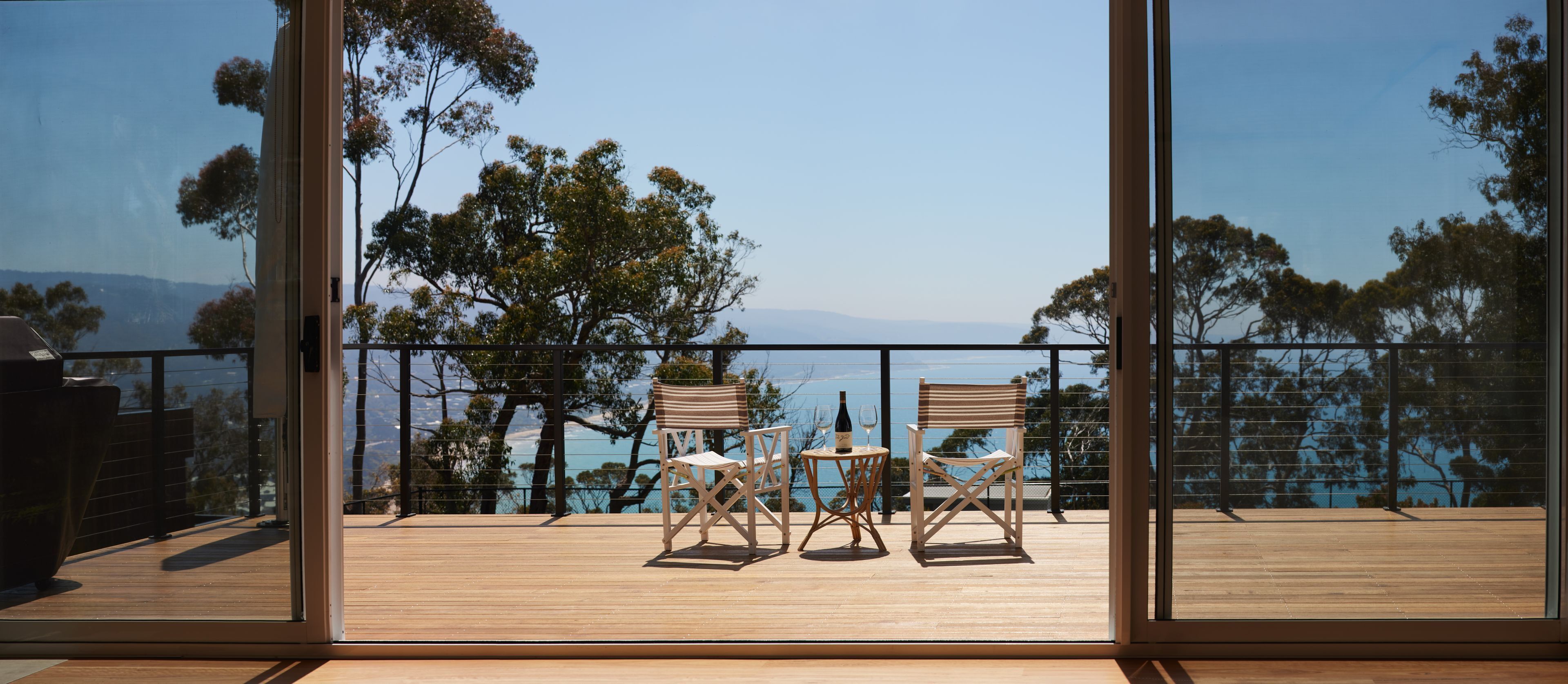 Ein Balkon mit zwei Stühlen und einem Tisch, der einen schönen Blick auf Bäume und ein Gewässer bietet.