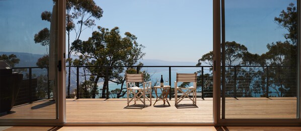 A balcony with two chairs and a table, overlooking a scenic view of trees and a body of water.