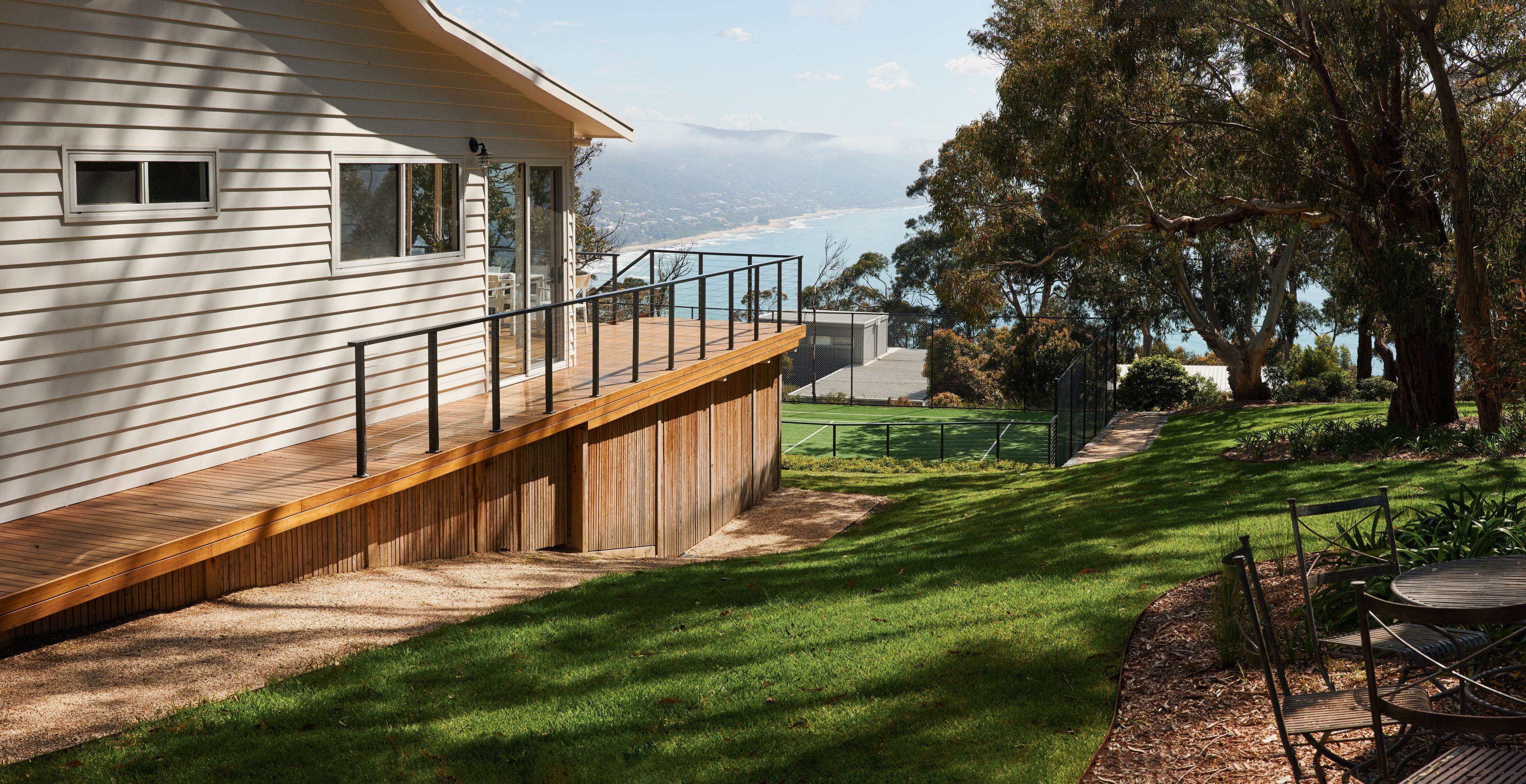 A residential property with a wooden deck, a tennis court, and a view of the ocean.
