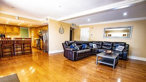 A living room with a sectional sofa, wooden flooring, a kitchen in the background, and a dining area with chairs. - FAMILY HOME W/POOL & BBQ NEAR LAS VEGAS STRIP 9 MINS (Las Vegas)