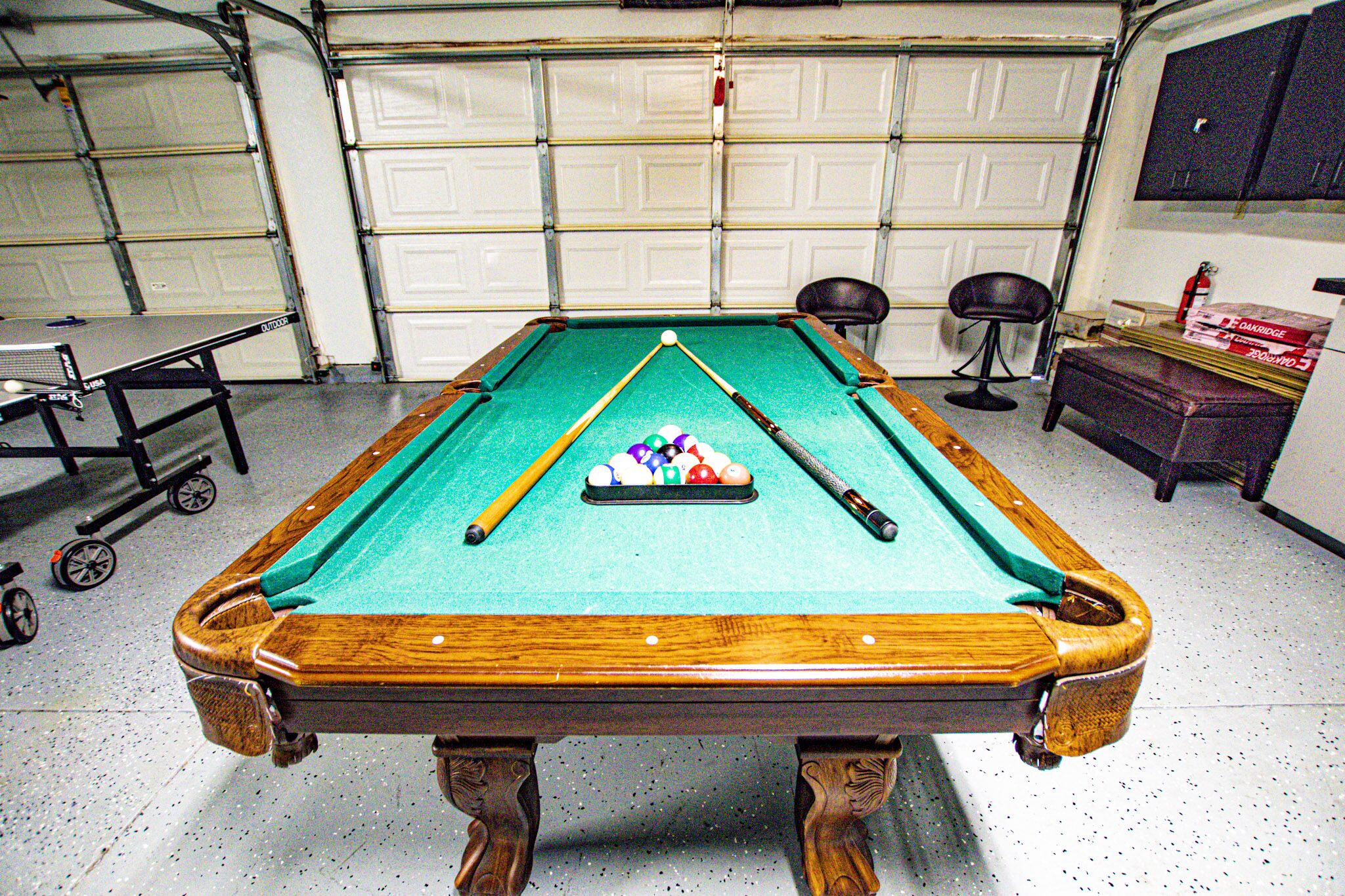Une table de billard dans un garage, recouverte d’un drap vert, et entourée d’un cadre en bois.
