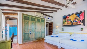 Ein Zimmer mit zwei Betten, einem Deckenventilator, einem Bild und einer Tür mit blauem Griff.