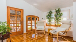 Ein Zimmer mit Fliesenboden, zwei Holzstühlen, einer Topfpflanze und einer Holztür mit Glasfeldern.