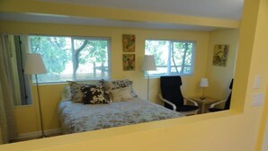 Una habitación con una cama, dos sillas y dos ventanas.
