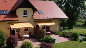Ein zweistöckiges Haus mit rotem Ziegeldach, einem kleinen Balkon und einer Terrasse mit Gartenmöbeln.