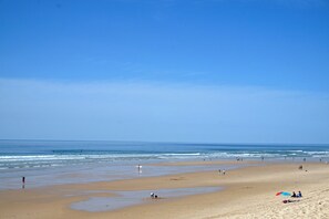 A wide beach with people walking and sitting, and a clear blue sky.