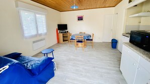 A room with a wooden ceiling, a dining table with chairs, a television, and a kitchen area with a microwave. - Small country house with ocean and shops on foot (045) (Biscarrosse)