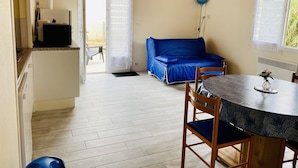 A room with a dining table, a blue sofa, and a kitchen area with a refrigerator. - Small country house with ocean and shops on foot (045) (Biscarrosse)