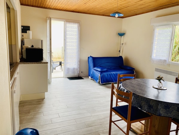 A room with a dining table, a blue sofa, and a kitchen area with a refrigerator.
