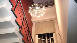 Uma escadaria com design geométrico, uma luminária moderna e uma janela com persianas.