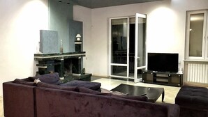 Sala de estar com sofá, lareira, televisão e porta de vidro deslizante para uma varanda.