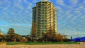 Un grand hôtel à plusieurs étages, doté de balcons, entouré d’arbres et bordé d’une zone sablonneuse.