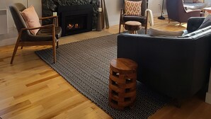 Una sala de estar con chimenea de piedra, piso de madera, sofá negro y alfombra estampada.