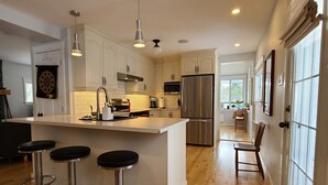 Una cocina moderna con una isla central, taburetes de bar, electrodomésticos de acero inoxidable y suelo de madera.