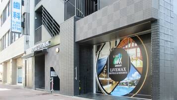 En moderne hotels facade med et tydeligt 'HOTEL LIVEMAX' skilt, en stor reklame for 'LIVE MAX GROUP LiVEMAX HOTELS & RESORTS' og et synligt telefonnummer (052-451-9796).
