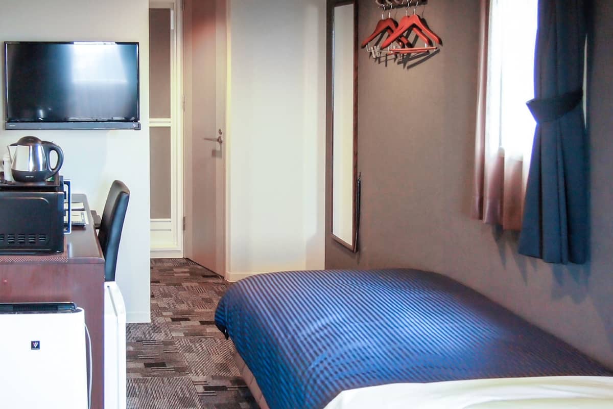 A hotel room with a bed, a desk with a computer, a television, and a coat rack.