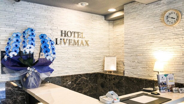 Un mostrador de recepción de hotel con encimera de mármol blanco, un reloj en la pared y un arreglo floral.