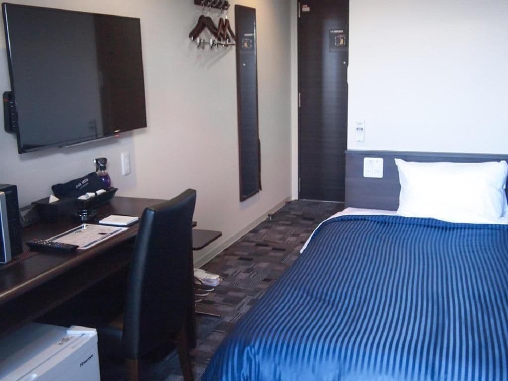 A hotel room with a bed, a desk, a chair, a television, and a coat rack.