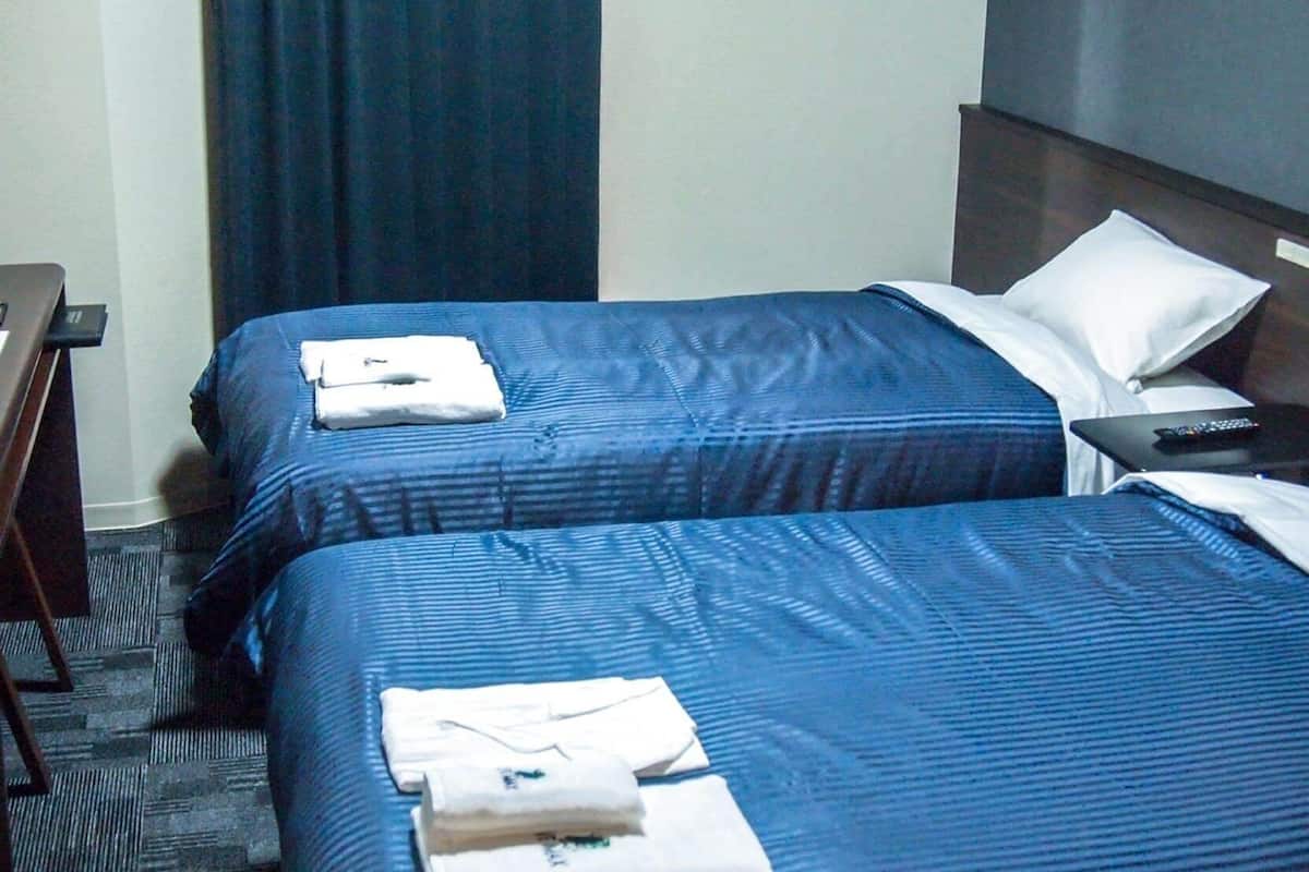 A hotel room with two beds, a desk, and a remote control on the nightstand.