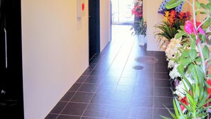 Un pasillo con piso de baldosas, una puerta al final y plantas en macetas a la derecha.