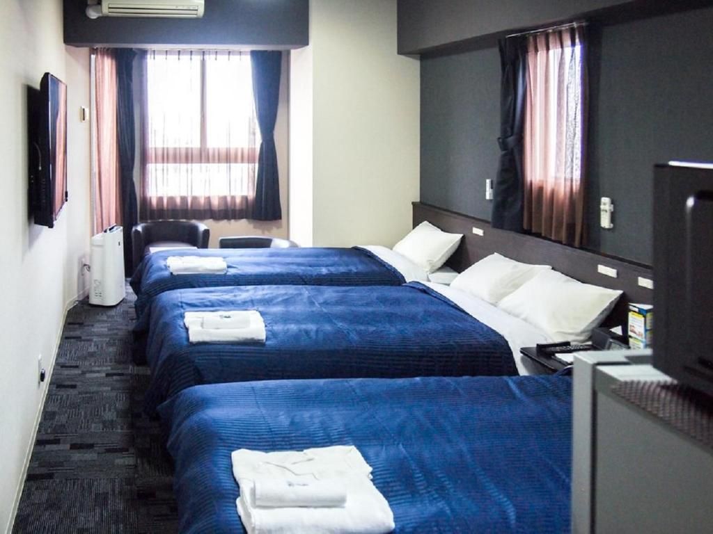 A hotel room with three beds, a desk, a chair, and a television.