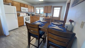 Une cuisine avec des meubles de rangement en bois, un réfrigérateur blanc, un four à micro-ondes, une cuisinière et une table à manger avec des chaises.