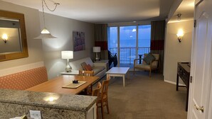 Habitación de hotel con comedor, sofá, silla, mesa y vista al mar.