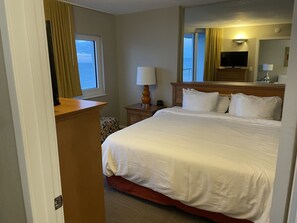 A hotel room with a large bed, a television, a desk with a lamp, and a window with curtains.