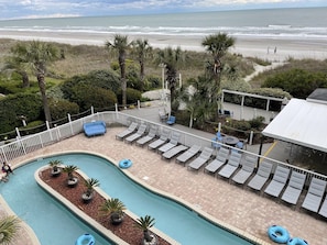 A pool area with lounge chairs and a view of the beach.