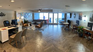 Un salón espacioso con suelo de madera en patrón de espiga, un sofá modular gris, una mesita redonda y un escritorio con computadora.