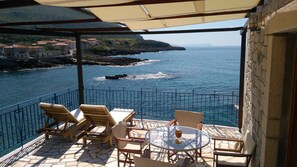 Eine Terrasse mit Meerblick, ausgestattet mit einem Tisch, Stühlen, einer Steinmauer und einem Metallgeländer.