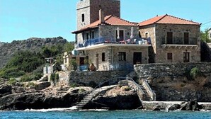 En bygning i sten med rødt tegltag, beliggende på en klippefyldt kyststrækning med udsigt til havet.